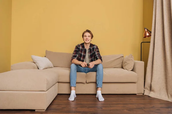Sonriente hombre sosteniendo mando a distancia y sentado en el sofá, fin del concepto de cuarentena - foto de stock