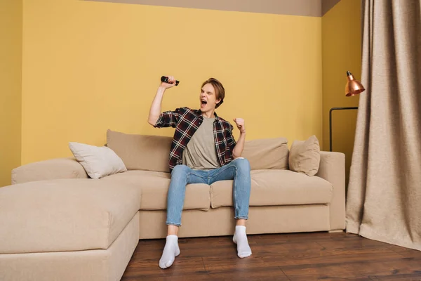 Homem animado sentado no sofá e segurando controlador remoto, fim do conceito de quarentena — Fotografia de Stock