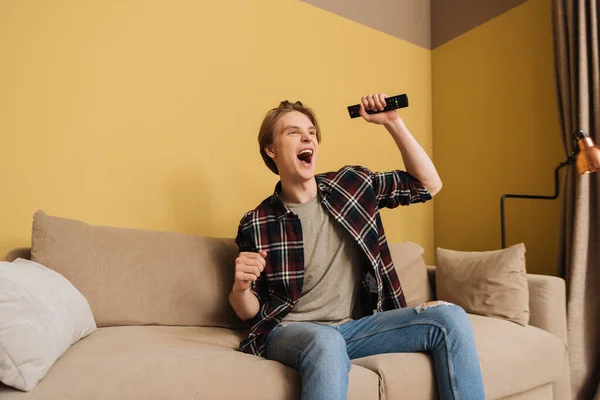 Excited man with opened mouth sitting on sofa and holding remote controller, end of quarantine concept — Stock Photo