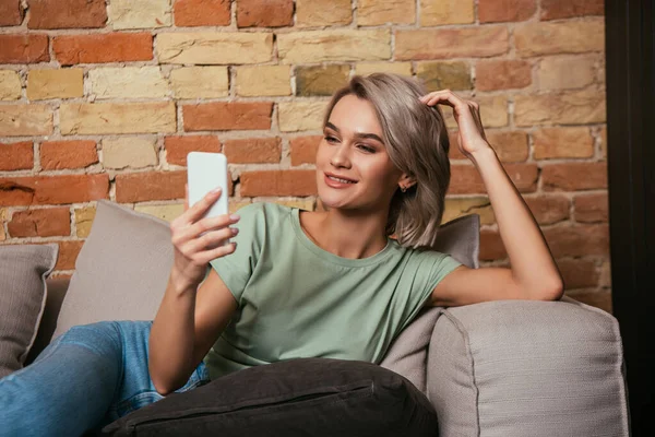 Glückliche junge Frau berührt bei Videoanruf auf Smartphone Haare — Stockfoto