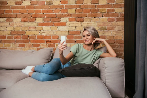 Felice giovane donna con video chat su smartphone mentre si rilassa sul divano — Foto stock