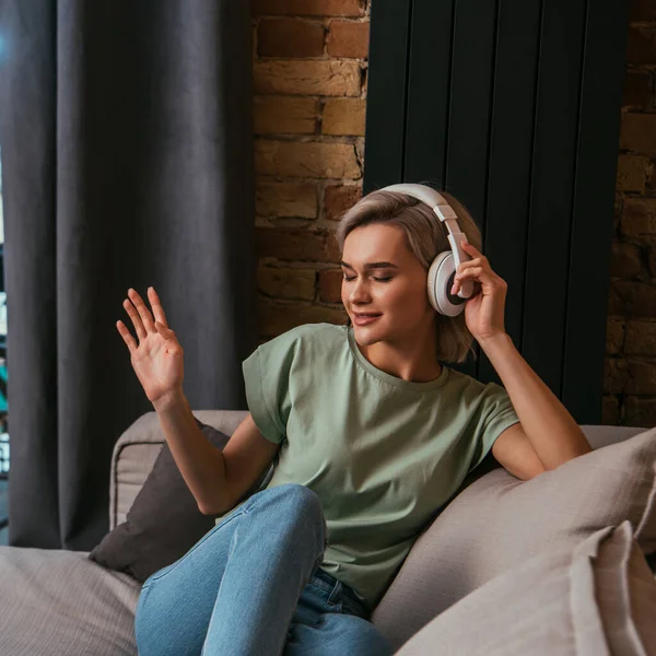 Attractive woman with closed eyes gesturing while listening music in wireless headphones — Stock Photo