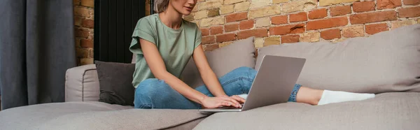 Cropped view of young woman using laptop while sitting on sofa at home, horizontal image — Stock Photo