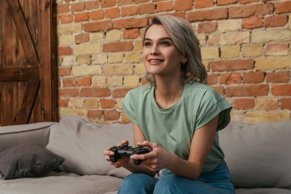 KYIV, UKRAINE - 30 de abril de 2020: mulher animada jogando videogame enquanto se senta no sofá em casa — Fotografia de Stock