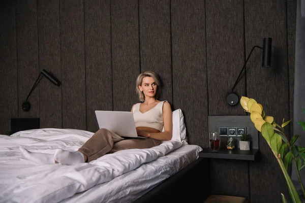 Attractive young woman looking away while using laptop in bedroom — Stock Photo