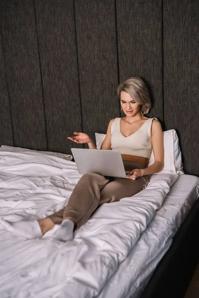 Verwirrte Frau zeigt Achselzucken-Geste bei Laptop-Nutzung im Schlafzimmer — Stockfoto