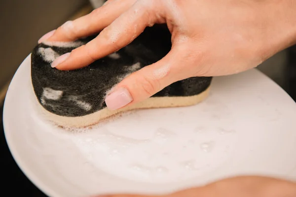 Обрізаний вид жінки, що миє білу тарілку з губкою — стокове фото