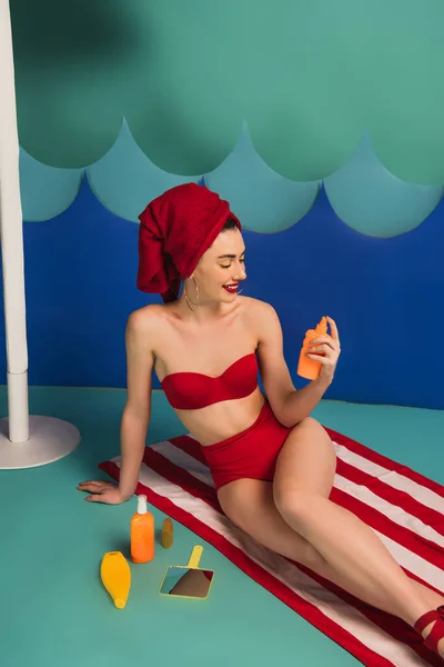 Femme heureuse en serviette rouge et maillot de bain tenant crème solaire près des vagues de coupe de papier — Photo de stock