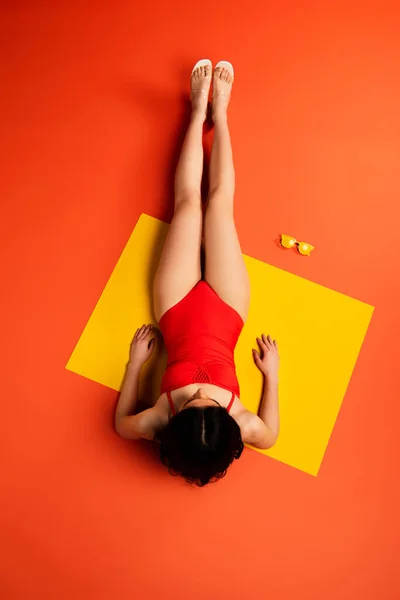Вид зверху дівчини, що лежить біля жовтих сонцезахисних окулярів на помаранчевому — стокове фото