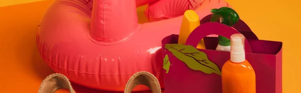 Concept panoramique de sac en papier avec crème solaire dans des bouteilles près anneau gonflable rose sur jaune — Photo de stock