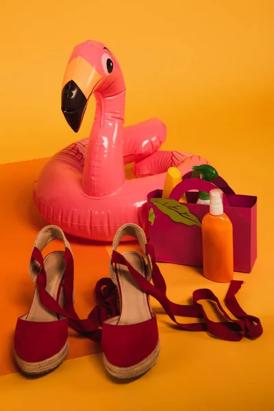 Паперовий мішок з сонцезахисним кремом у пляшках біля рожевого надувного кільця та взуття для платформи на жовтому — стокове фото