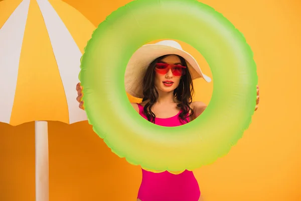 Stylische Frau mit Strohhut, Sonnenbrille und Badeanzug mit aufblasbarem Ring auf gelb — Stockfoto