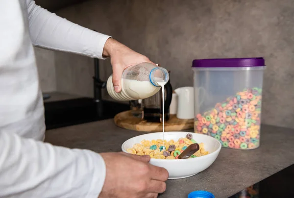 Обрезанный вид человека, наливающего молоко в миску с хлопьями во время приготовления завтрака — стоковое фото