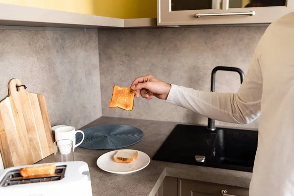 Cropped view of man holding tasty fried bread near toaster in kitchen — Stock Photo