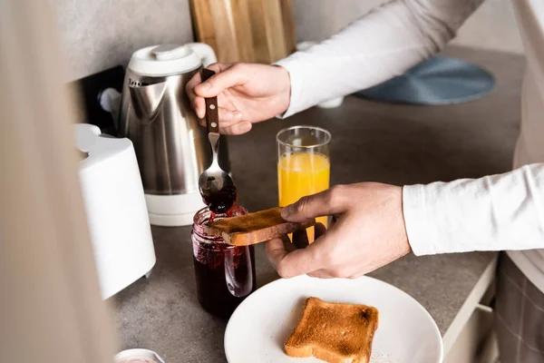 Teilansicht eines Mannes, der Marmelade auf Toast zum Frühstück verteilt — Stockfoto