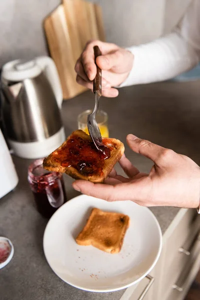 Vue recadrée de l'homme écartant la confiture sur le pain grillé pour le petit déjeuner — Photo de stock