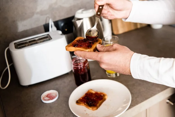 Vista recortada del hombre extendiendo mermelada en tostadas con cuchara - foto de stock