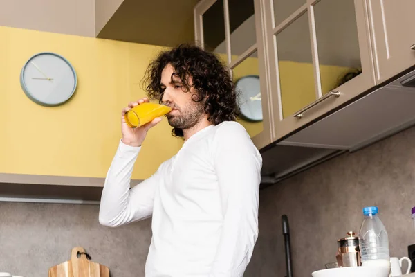 Низкий угол зрения вдумчивый человек пьет апельсиновый сок, стоя на кухне — стоковое фото