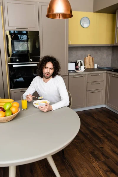 Sorprendido hombre charlando en el teléfono inteligente durante el desayuno en la cocina - foto de stock