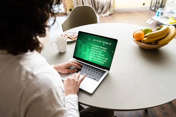 Back view of freelancer using laptop with medical website near fruits, coffee cup and plate with toasts — Stock Photo