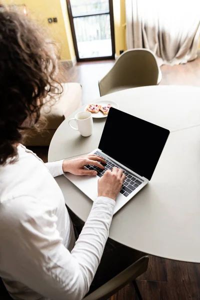 Back view of freelancer using laptop with blank screen near coffee cup and plate with toasts — Stock Photo