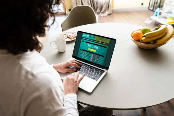 Back view of freelancer using laptop with Sportsbet website near fruits, coffee cup and plate with toasts — Stock Photo