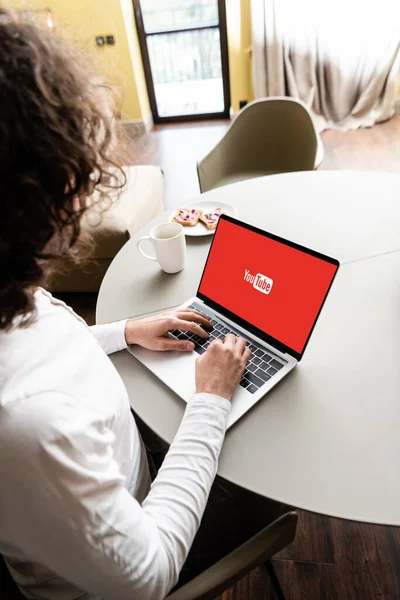 KYIV, UKRAINE - APRIL 25, 2020: high angle view of freelancer using laptop with Netflix on screen near coffee cup and plate with toasts — Stock Photo