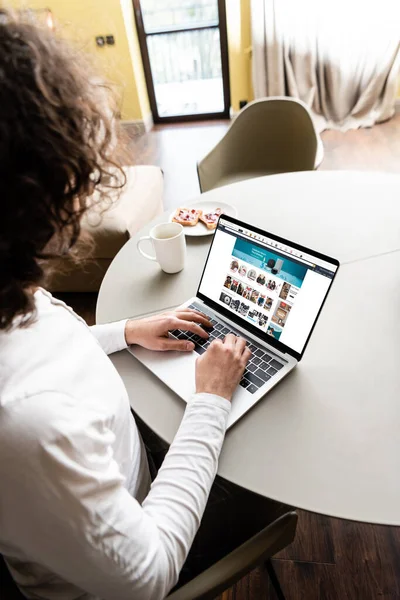 KYIV, UKRAINE - APRIL 25, 2020: High angle view of freelancer using laptop with Amazon website on sreen near coffer cup and plate with toasters — стокове фото