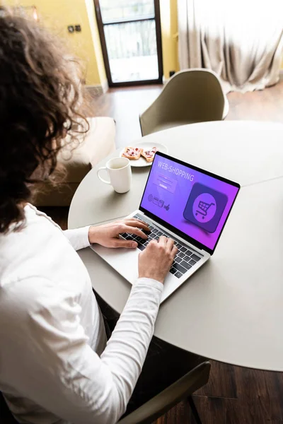 High angle view of freelancer using laptop with web shopping website near coffee cup and plate with toasts — Stock Photo