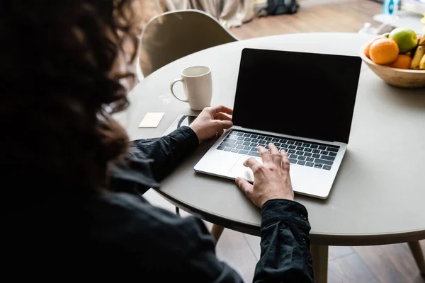 Back view of freelancer using laptop with blank screen near coffee cup, sticky notes and fruits — Stock Photo