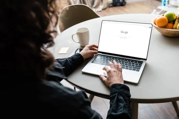 KYIV, UKRAINE - 25 AVRIL 2020 : vue arrière du pigiste à l'aide d'un ordinateur portable avec Google à l'écran près d'une tasse de café, des notes collantes et des fruits — Photo de stock