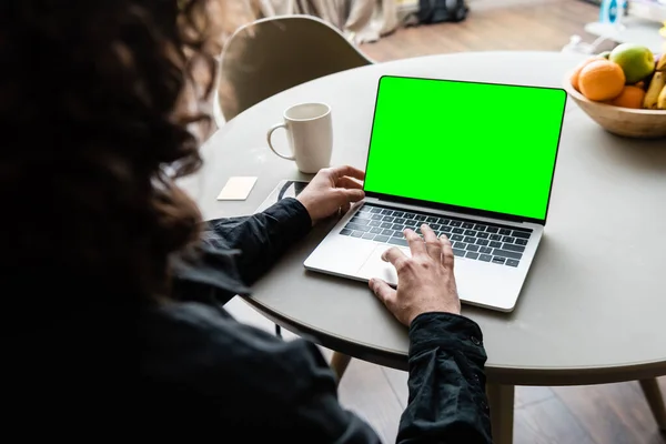 Back view of freelancer using laptop with green screen near coffee cup, sticky notes and fruits — Stock Photo