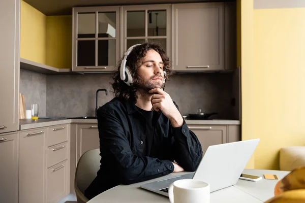 Concentration sélective de l'homme dans les écouteurs regardant l'ordinateur portable pendant le webinaire dans la cuisine — Photo de stock