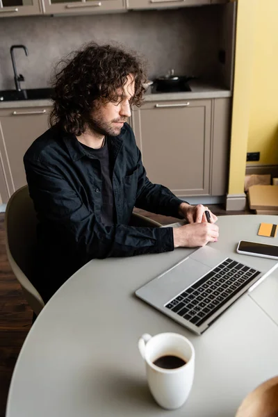 Selective focus of man writing near digital devices and credit card during webinar in kitchen — Stock Photo