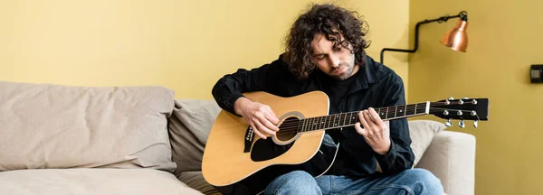 Panorâmica tiro de homem bonito tocando guitarra acústica no sofá — Fotografia de Stock