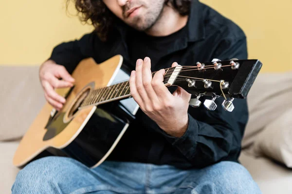 Обрезанный вид человека, выступающего на акустической гитаре на диване — стоковое фото