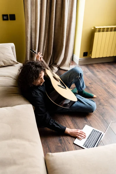 Vista aerea dell'uomo che tiene la chitarra acustica e usa il computer portatile durante il webinar sul pavimento a casa — Foto stock