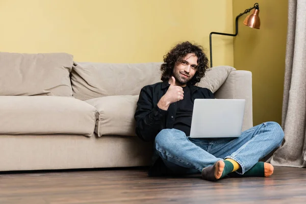Low angle view of handsome man showing thumb up while working on laptop on floor — Stock Photo