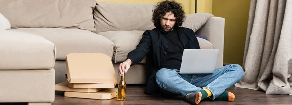 Panoramaorientierung eines Telearbeiters, der eine Bierflasche nimmt, während er Laptop in der Nähe von Pizzakartons auf dem Boden benutzt — Stockfoto