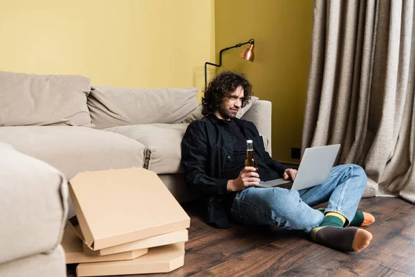 Enfoque selectivo de cajas de pizza cerca de freelancer usando laptop y sosteniendo cerveza en el piso - foto de stock