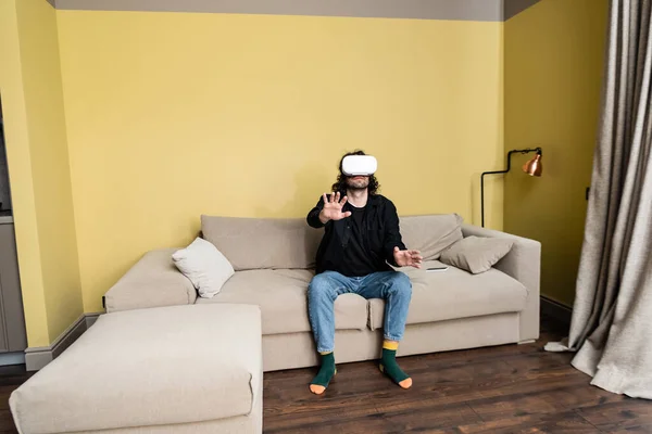 Curly man playing video game in virtual reality headset on couch — Stock Photo
