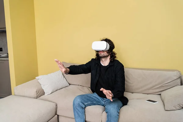 Man in virtual reality headset playing video game on sofa at home — Stock Photo