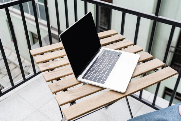 Ausgeschnittene Ansicht eines Mannes in der Nähe eines Laptops mit leerem Bildschirm auf einem Tisch auf dem Balkon — Stockfoto