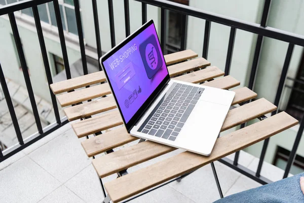 Ausgeschnittene Ansicht von Mann sitzt in der Nähe von Laptop mit Web-Shopping-Website auf dem Balkon — Stockfoto