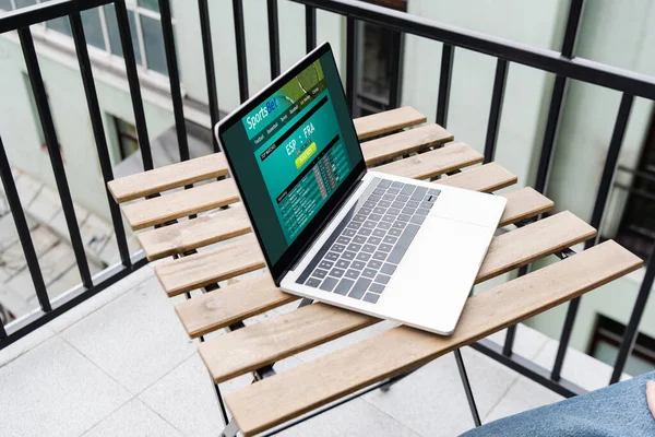 Обрезанный вид ноутбука с сайта спортивной ставки и человека, сидящего на балконе — стоковое фото