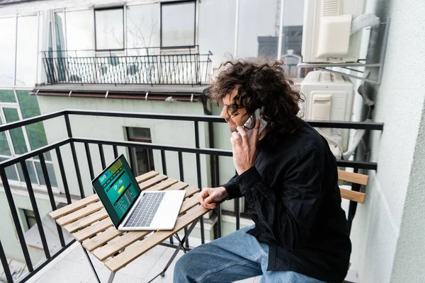 Hombre hablando en el teléfono inteligente cerca de la computadora portátil con deportes sitio web de apuestas en balcón - foto de stock