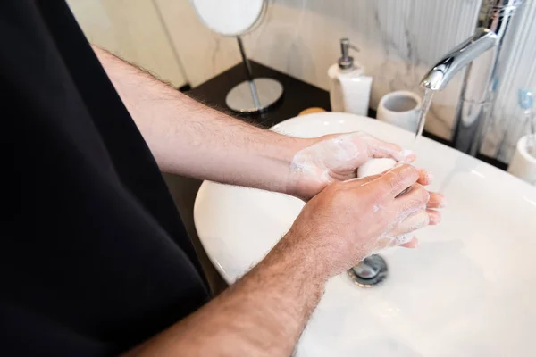 Vista recortada del hombre sosteniendo jabón mientras se lava las manos en el baño - foto de stock
