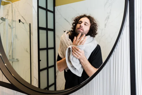 Красивый мужчина смотрит в зеркало, держа полотенце в ванной — стоковое фото