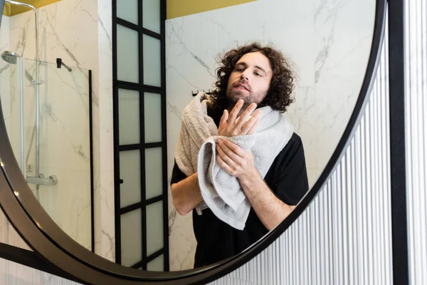 Handsome man looking at mirror while holding towel in bathroom — Stock Photo