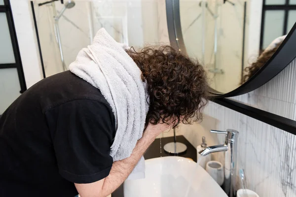 Вид збоку кучерявий чоловік миє обличчя у ванній — стокове фото